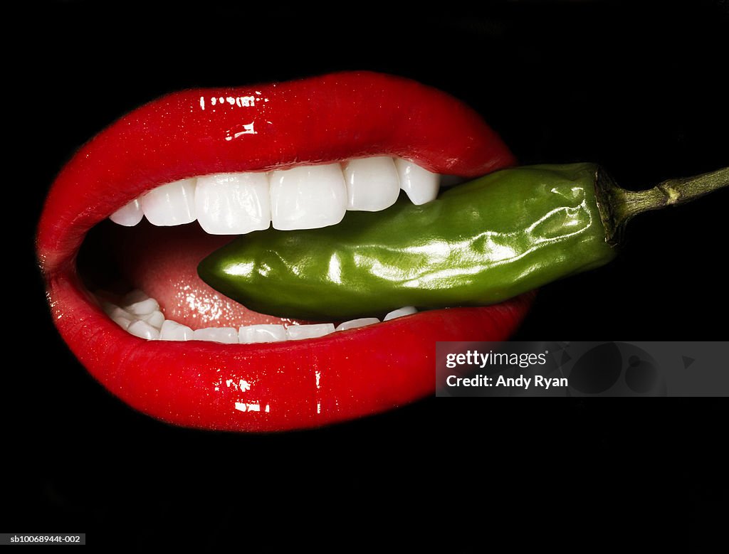 Mouth biting Jalepeno pepper, close-up, studio shot