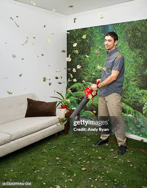 young man blowing leaves in living room decorated with nature - leaf blower stock pictures, royalty-free photos & images