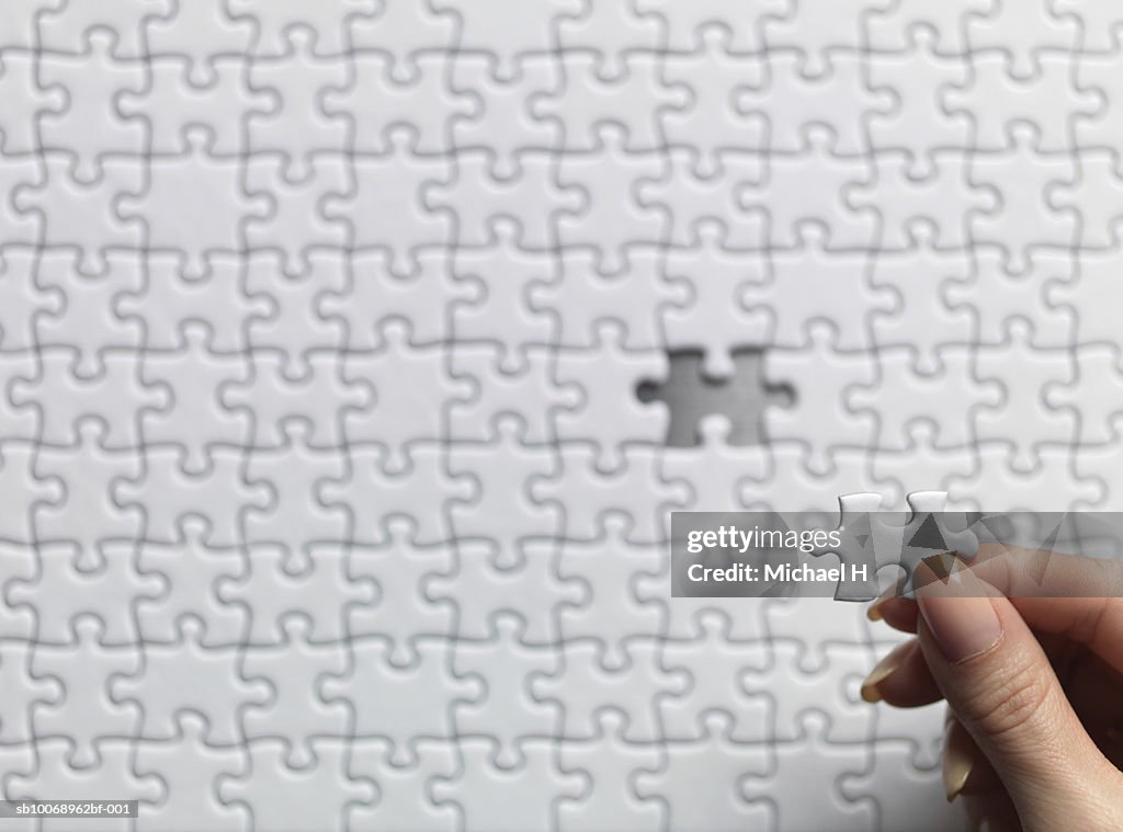 Woman holding one jigsaw piece over puzzle