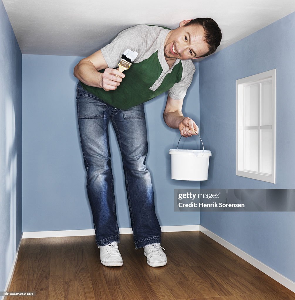 Man painting low ceiling room, smiling, portrait