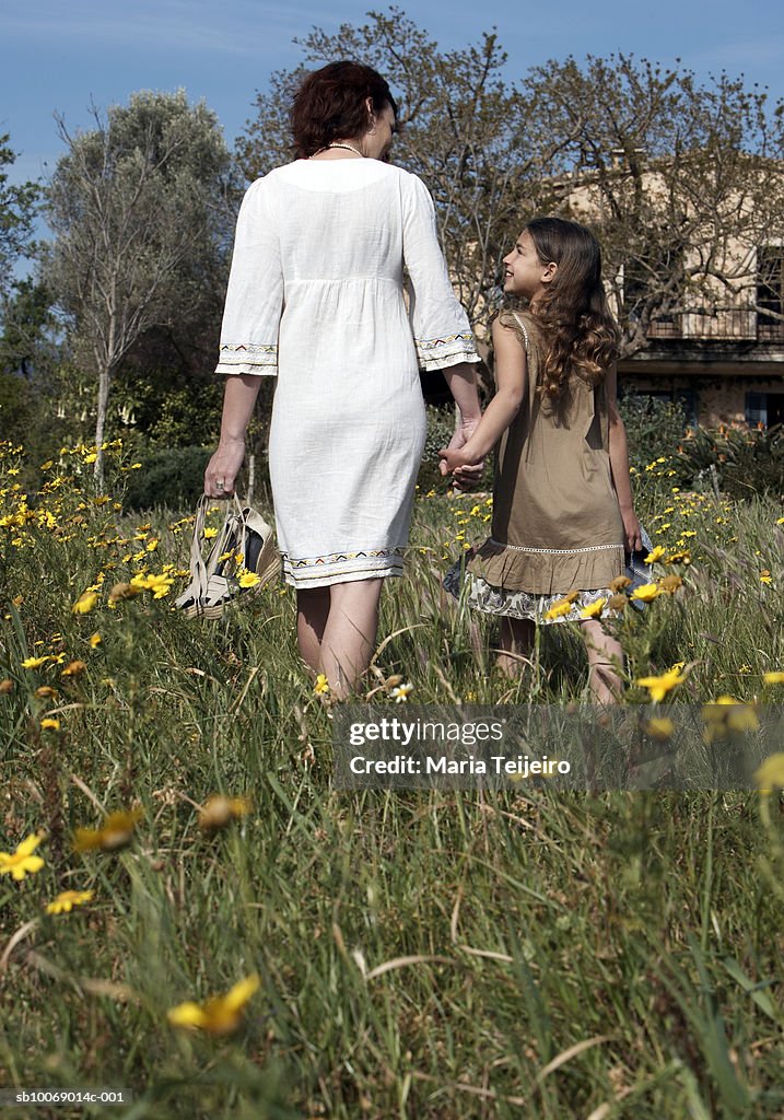 Mother and daughter (8-9) walking in meadow, rear view