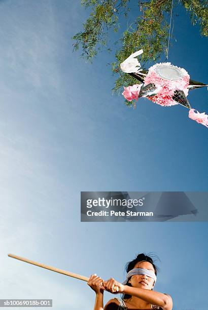 mid adult woman swinging stick at pinata hanging from tree - pinata photos et images de collection