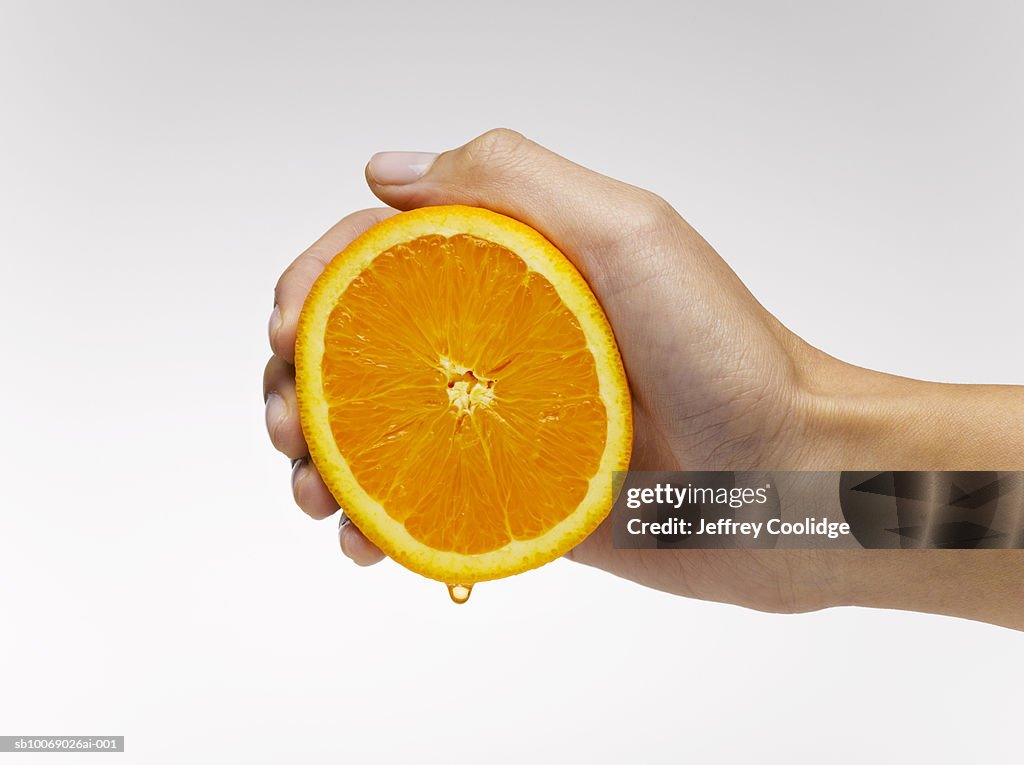 Woman's hand squeezing orange slice, studio shot