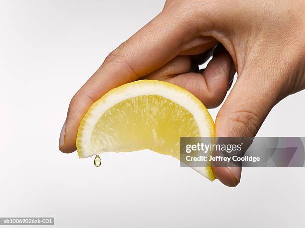 woman's hand holding lemon slice, studio shot - estrujar fotografías e imágenes de stock