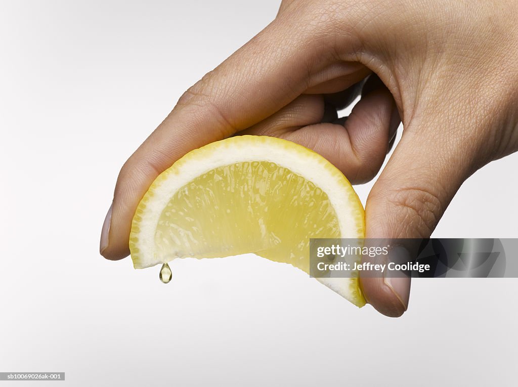 Woman's hand holding lemon slice, studio shot