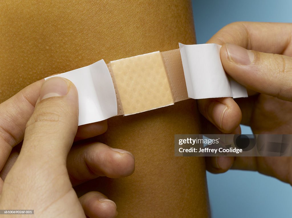 Woman placing bandage on man's arm, close-up, studio shot