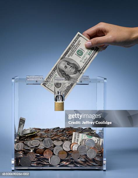 woman's hand placing dollar bill into collection box filled with money, studio shot - money lock box stock pictures, royalty-free photos & images
