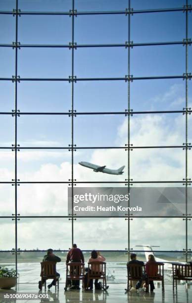 people sitting in airport lobby and looking at airplane taking off - vertikal stock-fotos und bilder
