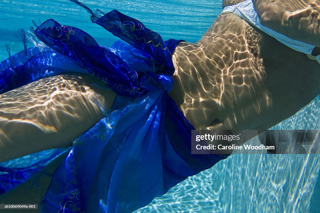 Mid adult woman in sarong swimming, mid section, underwater view