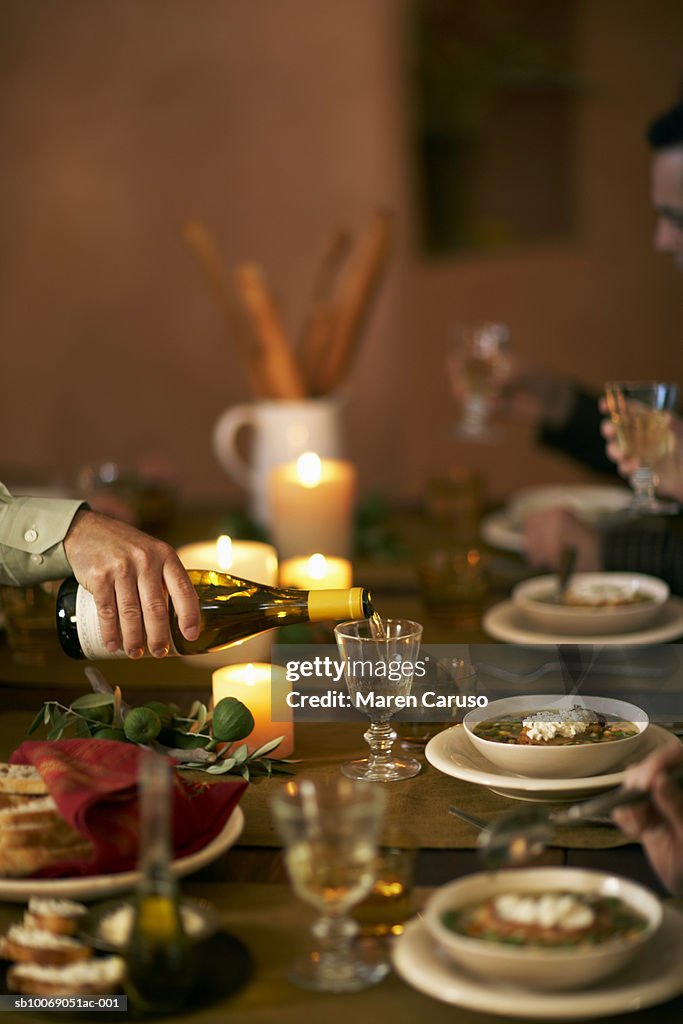 Bowls of soup on dinning table and man pouring wine into glass