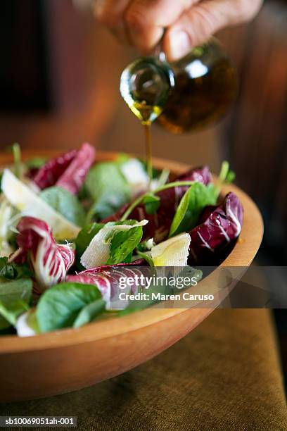 person pouring oil onto salad in wooden bowl, close-up - olive oil bowl stock pictures, royalty-free photos & images