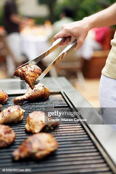 woman holding barbecuing chicken on grill with tongs, close-up - kip stockfoto's en -beelden