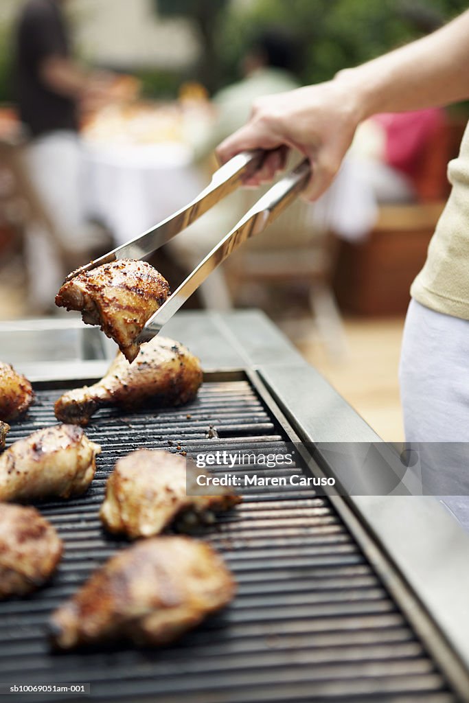 Woman holding barbecuing chicken on grill with tongs, close-up