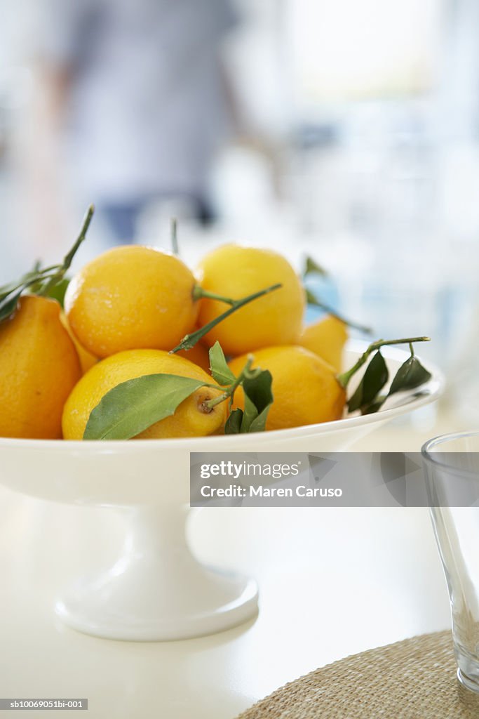 Lemons in bowl on table, person standing in backgroundclose-up