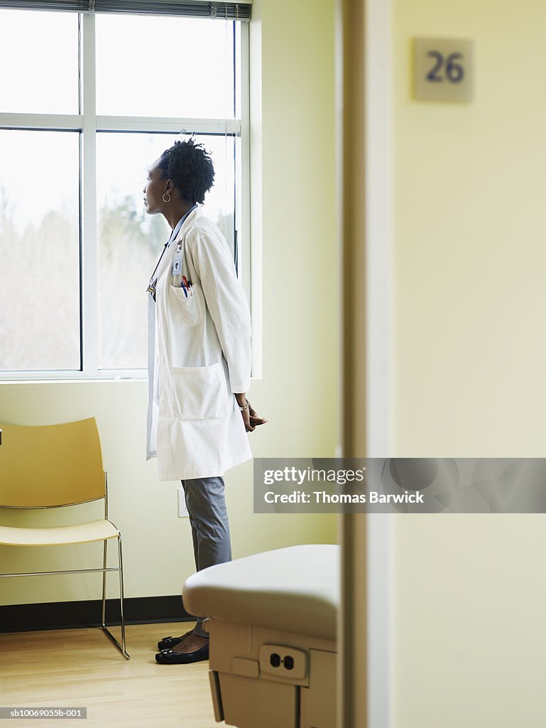 Female doctor standing in exam room looking out window