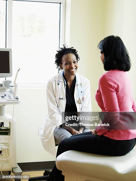 female doctor talking to woman in exam room, smiling - black female doctor stock-fotos und bilder