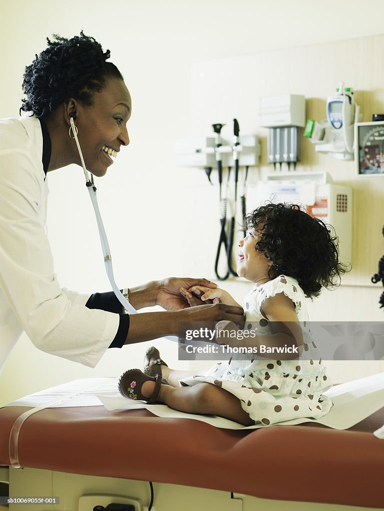 Female doctor examining baby girl (12-17months) with stethoscope, smiling