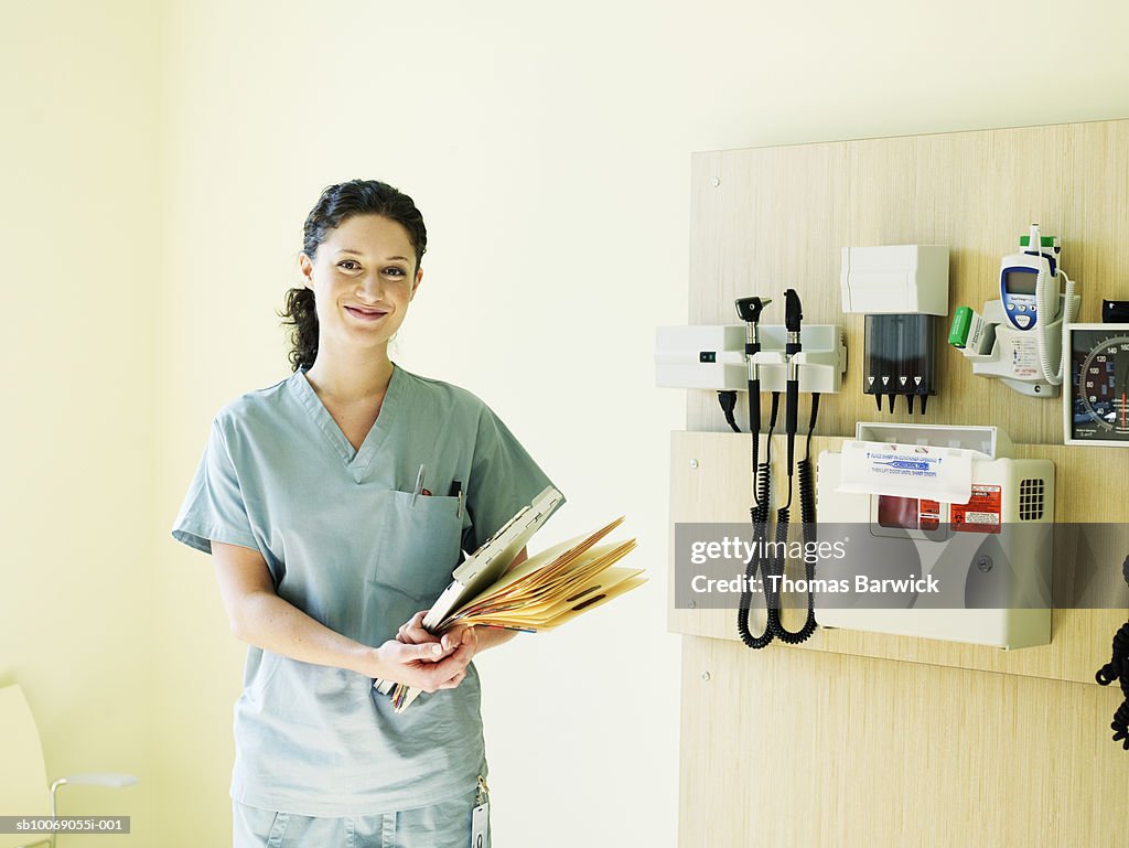 Female nurse in exam room holding file, smiling, portrait