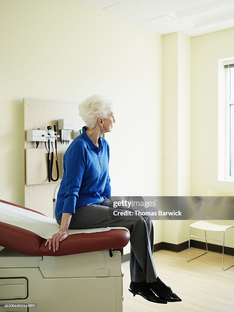 Senior woman sitting on examination table, looking away