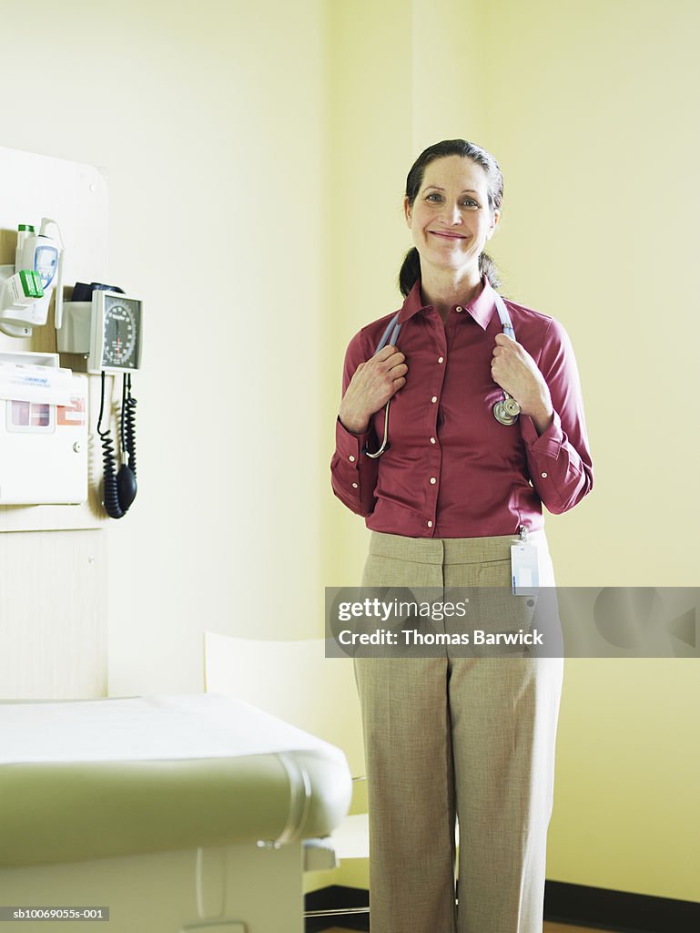 Female doctor in exam room holding stethoscope, smiling, portrait