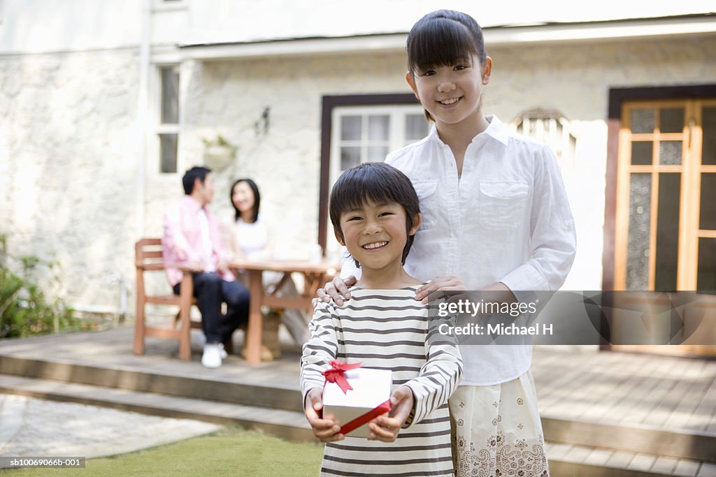 Portrait of sister (12-13) and brother (6-7) with gift outside house