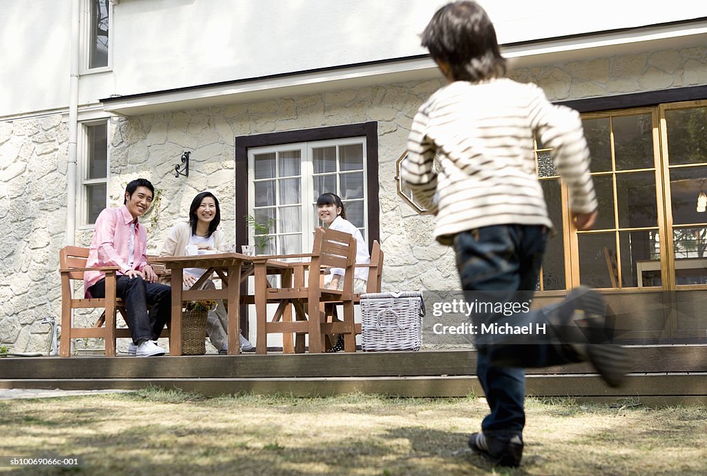 Boy (6-7) running towards family sitting outside house (blurred motion)