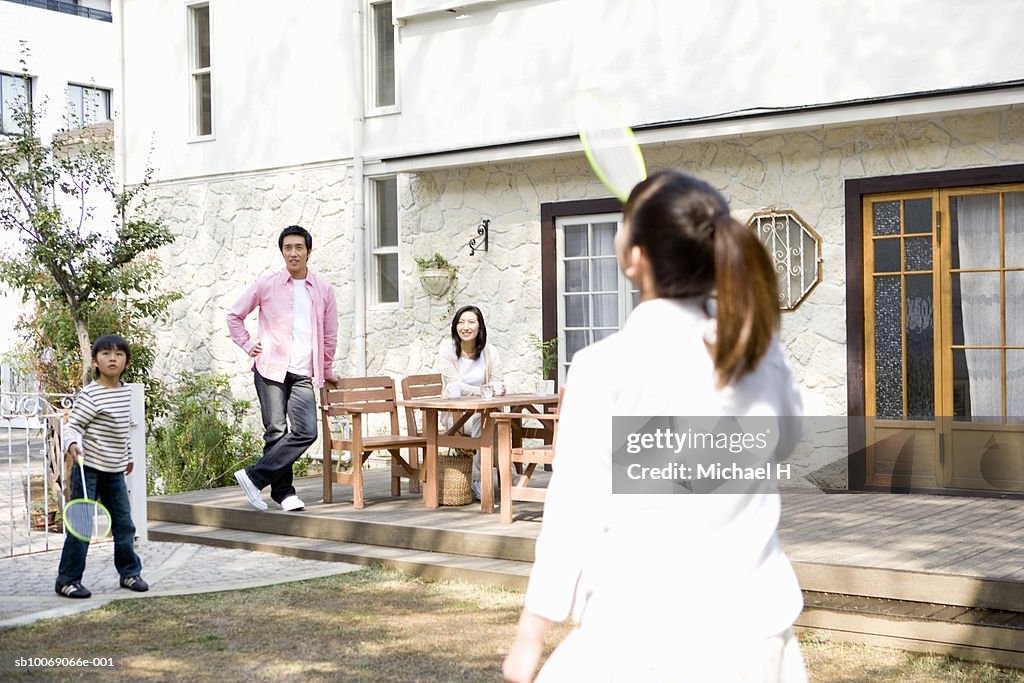 Parents watching son and daughter (6-13) play badminton outside house