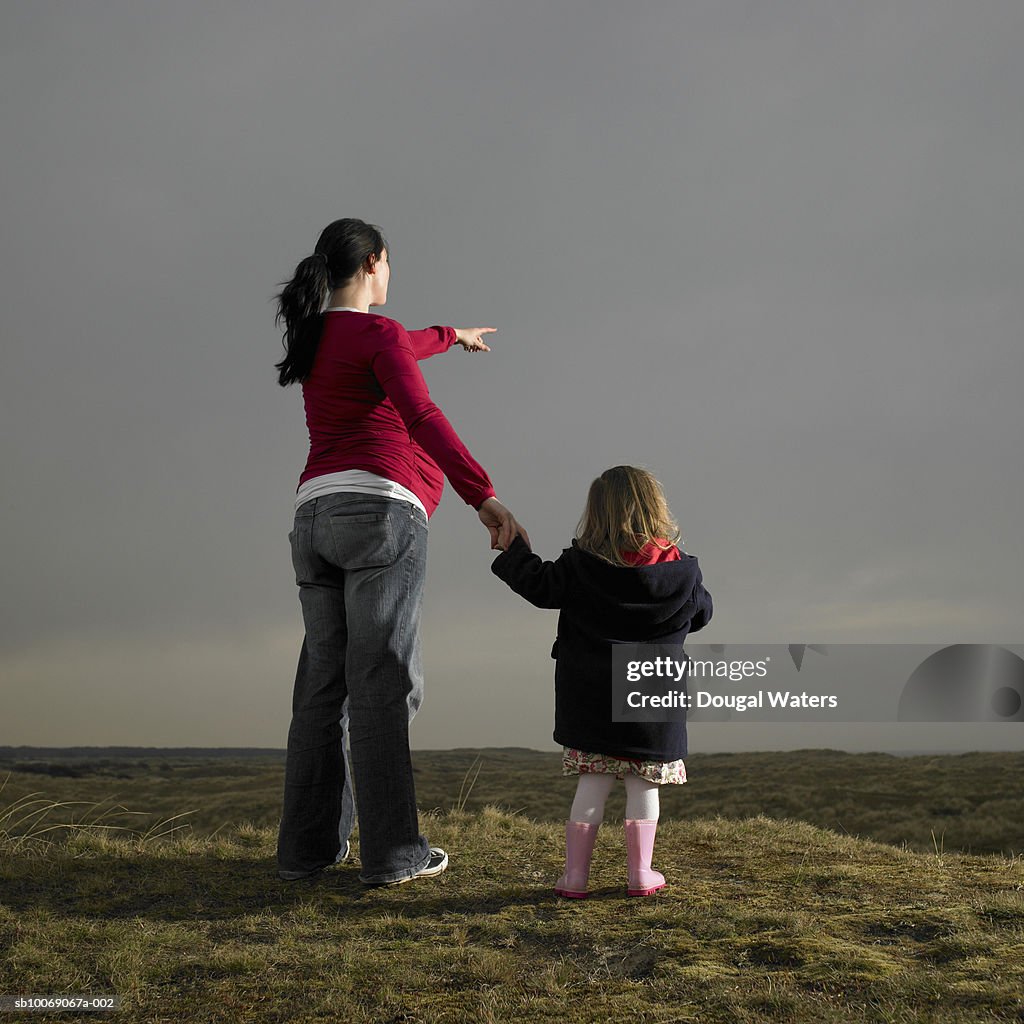 Pregnant woman and daughter (2-3) standing on heath land, rear view