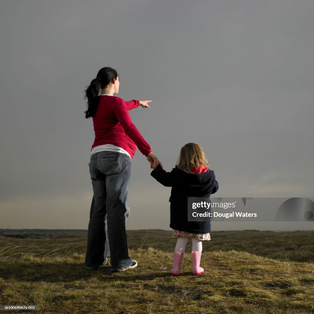 Pregnant woman and daughter (2-3) standing on heath land, rear view