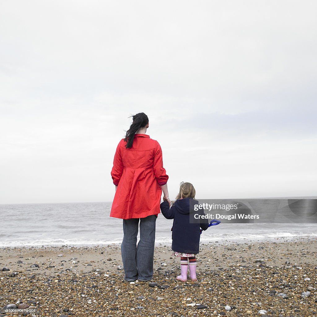 Woman and daughter (2-3) standing on beach, rear view