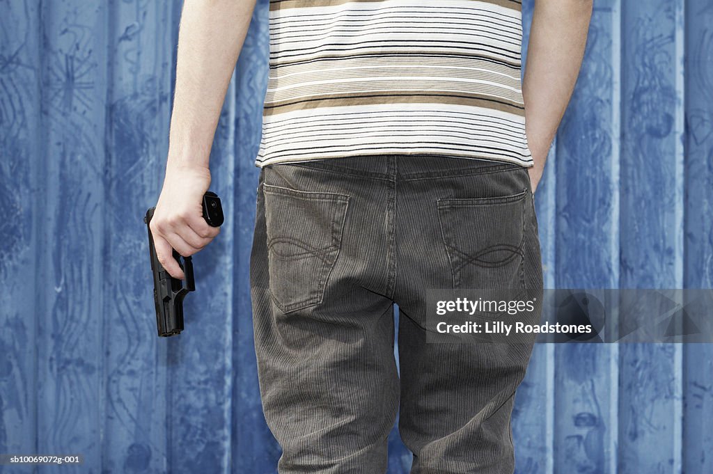 Young man holding gun, close-up, mid section