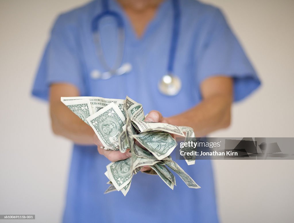 Female doctor holding US dollars, mid section