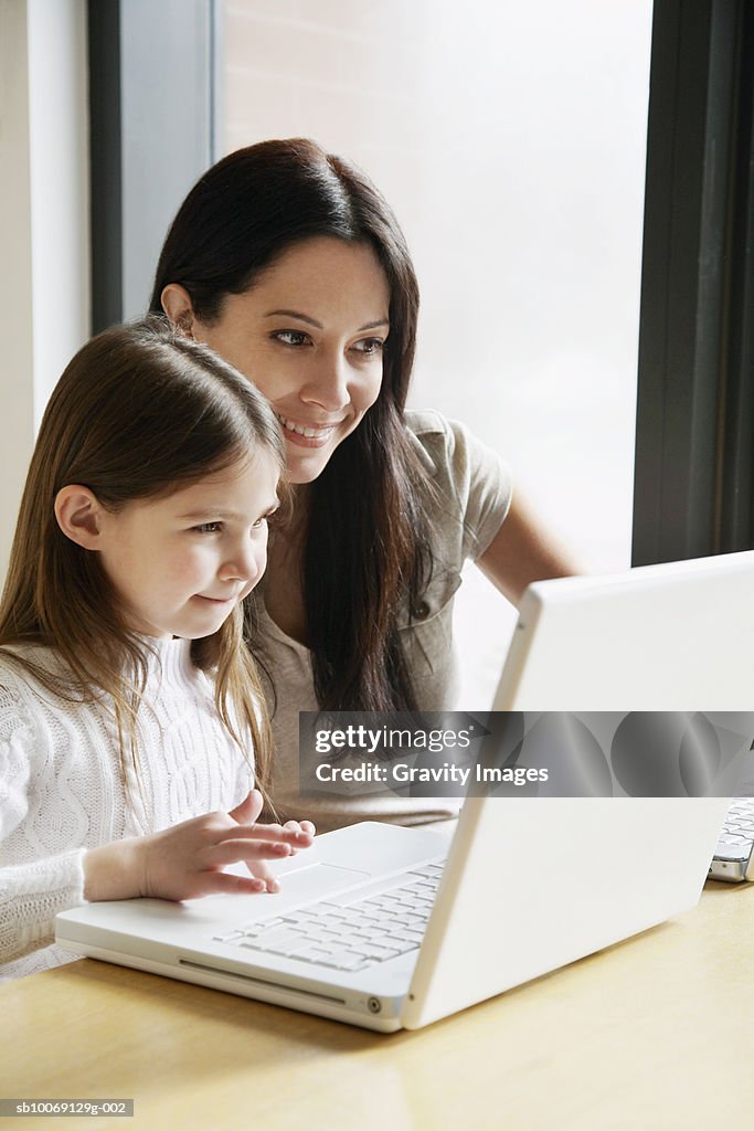 Mother and daughter (8-9) using laptop, smiling