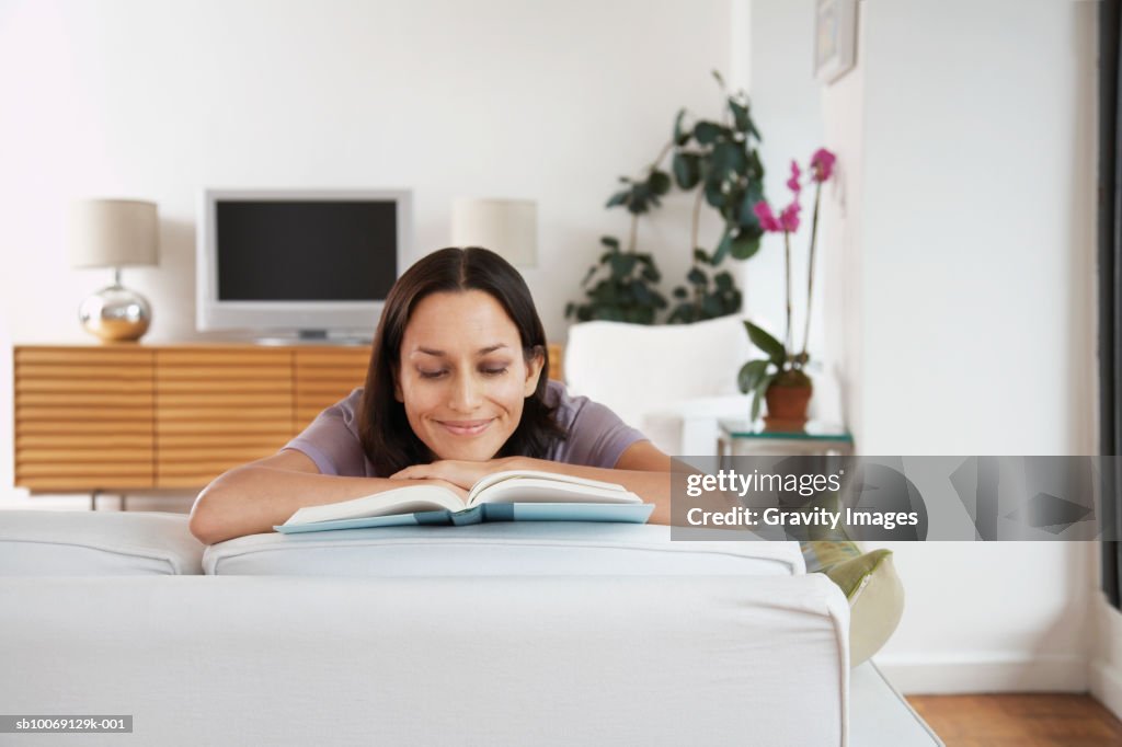 Woman reading book in living room, smiling