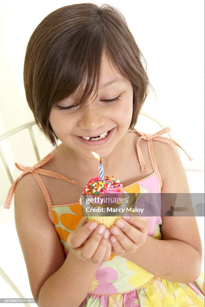 Girl (6-7) holding cupcake with lit candle