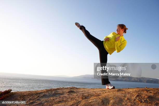 young woman practicing high kick on shore - hög spark bildbanksfoton och bilder