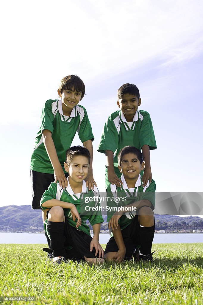 Four boys in soccer uniforms standing on field, portrait