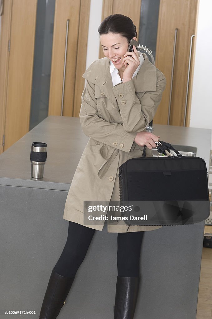 Woman in trench coat using mobile phone in lobby