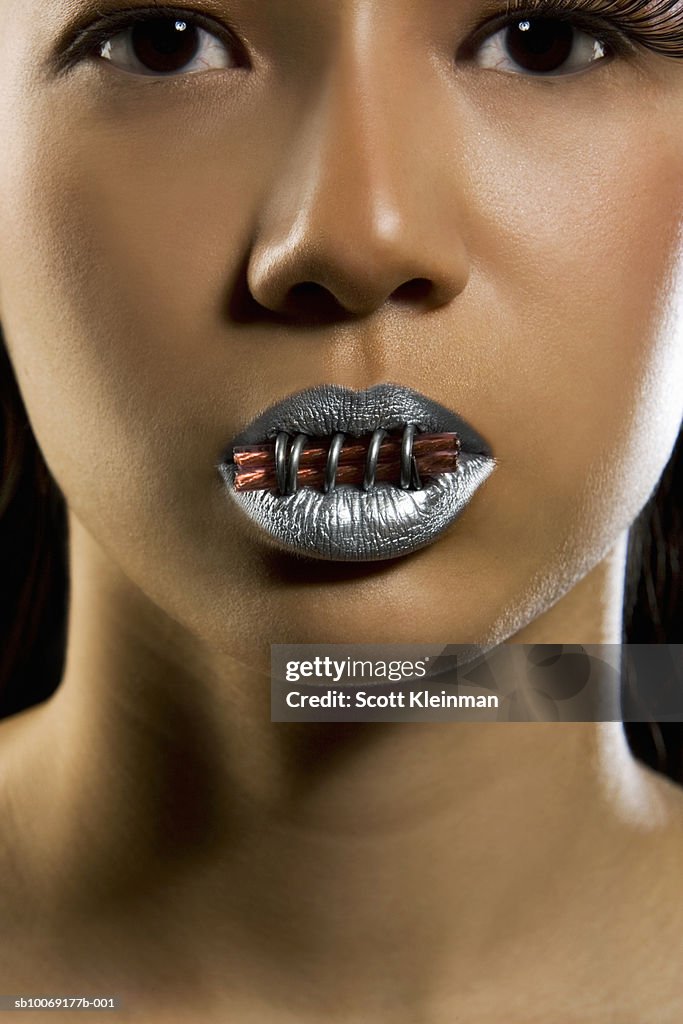 Woman with silver lipstick with electric wire in mouth