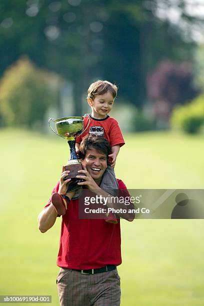 father with son (2-3 years) on shoulders, holding trophy on golf course - holding trophy cup stock pictures, royalty-free photos & images