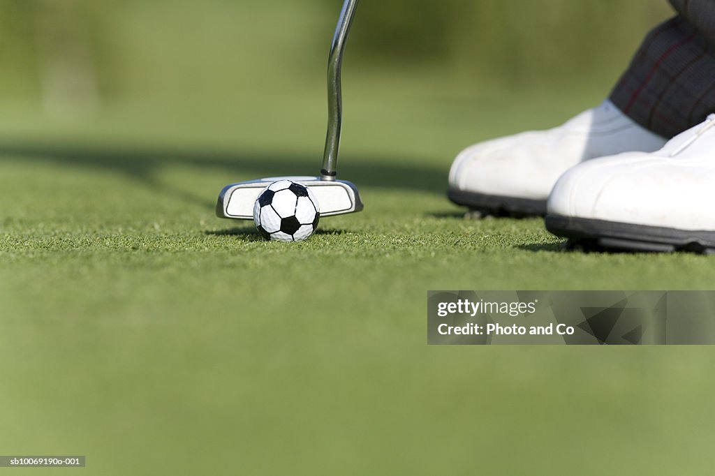 Male golfer putting soccer golf ball on green, low section, close up