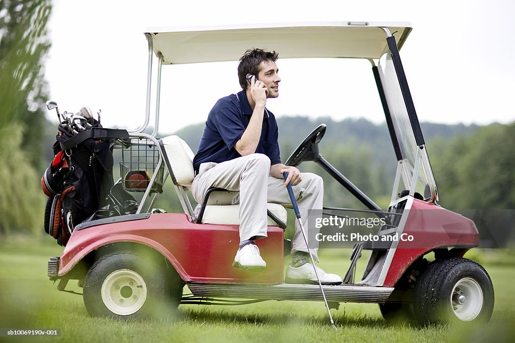 France, Dordogne, male golfer using mobile phone in golf cart