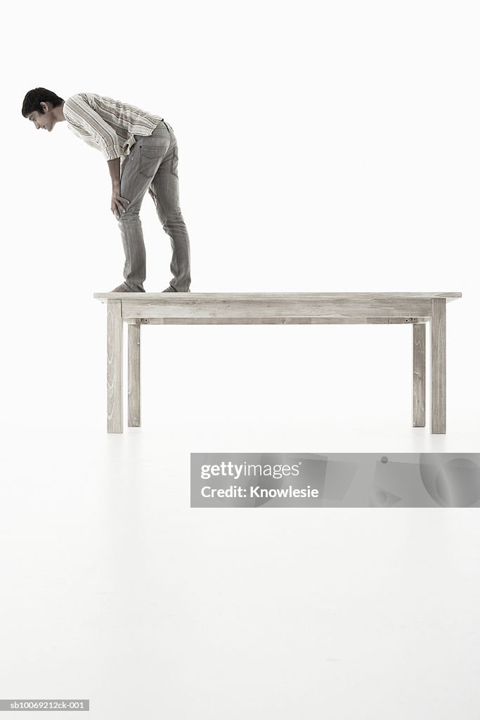 Man standing on wooden table looking down against white background, side view
