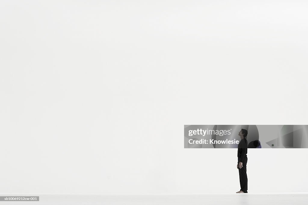 Homem de pé em distância com fundo branco, vista lateral