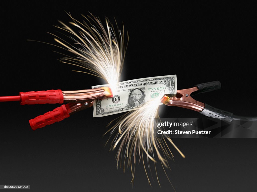 Sparks coming off US dollar bill attached to jumper cables