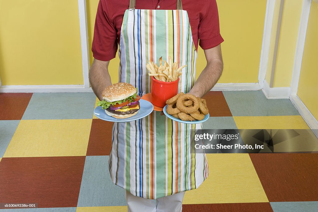 Mid section of waiter holding French fires, hamburger and donuts