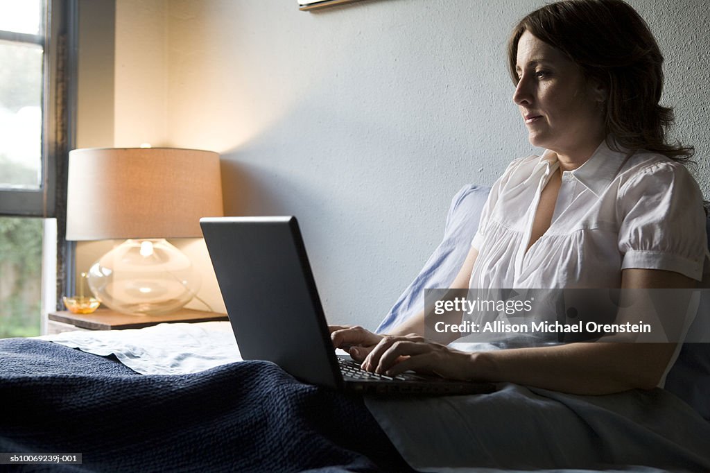 Woman sitting on bed using laptop