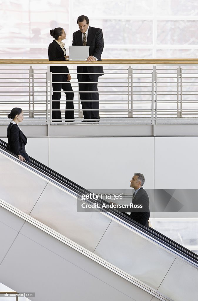 Business women and man working on laptop, man and woman on escalator in foreground