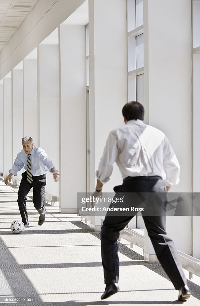 Two business men playing with soccer ball in office