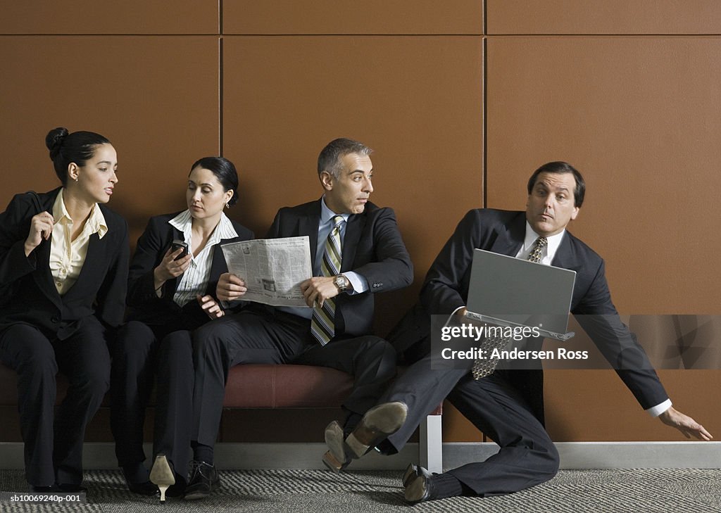 Business man with laptop getting pushed off from bench by businesspeople